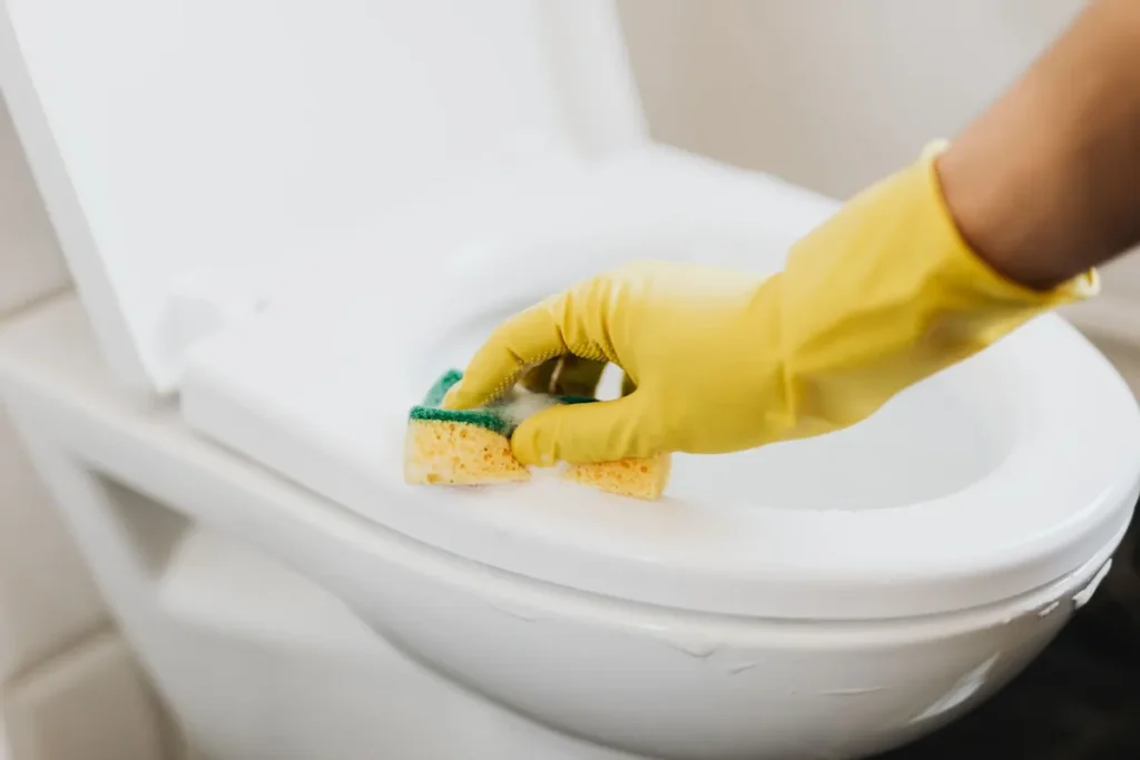 Hand in een gele handschoen maakt een toiletpot schoon met een spons